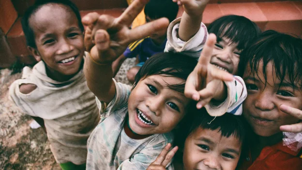 Gruppo di bambini sorridenti che fanno il segno della pace con le mani, in un contesto allegro e spensierato