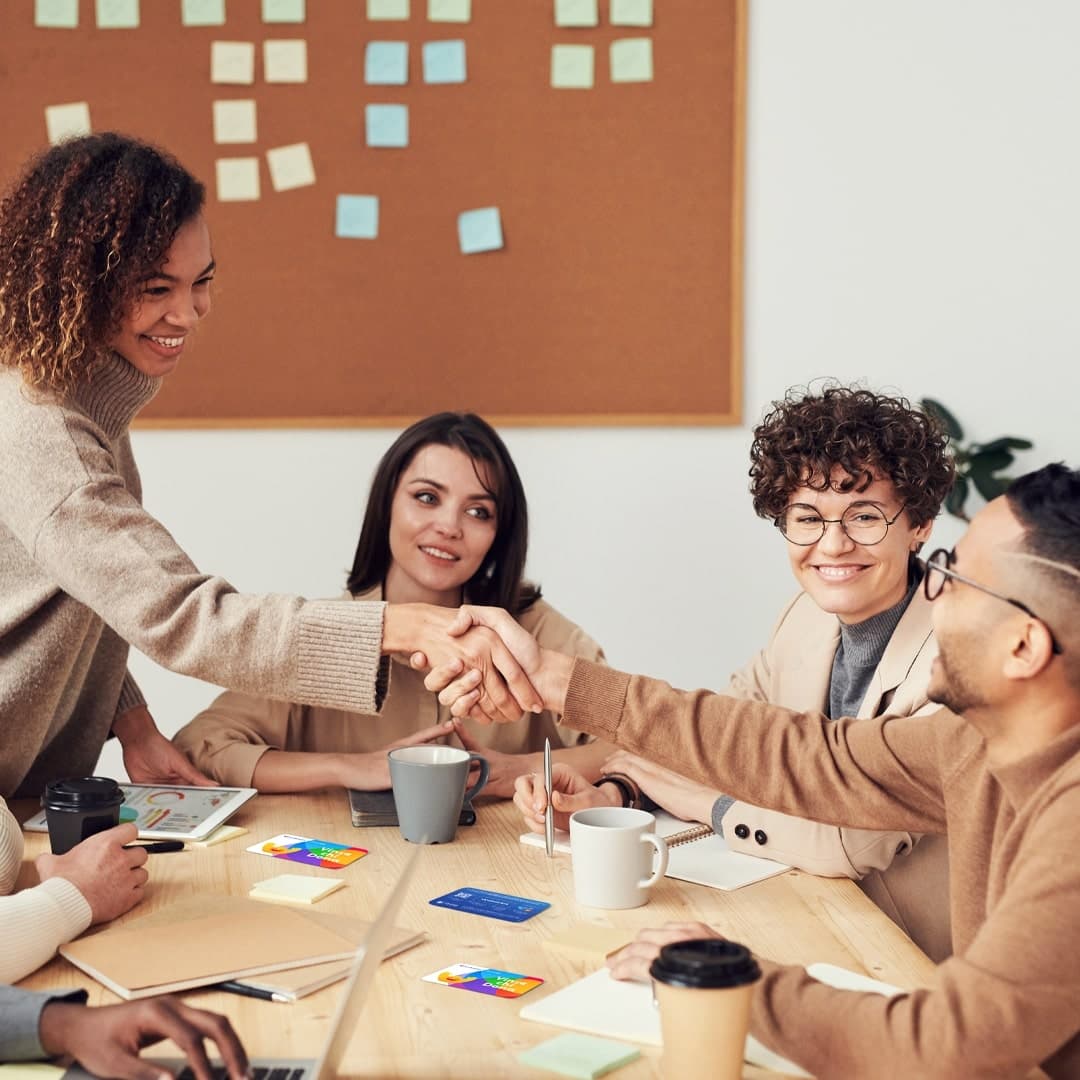 Team di professionisti in un ambiente di lavoro collaborativo, mentre due persone si stringono la mano con un sorriso, simbolo di accordo e cooperazione